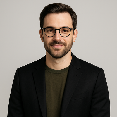 Man wearing glasses and a black blazer over a green shirt on a gray background